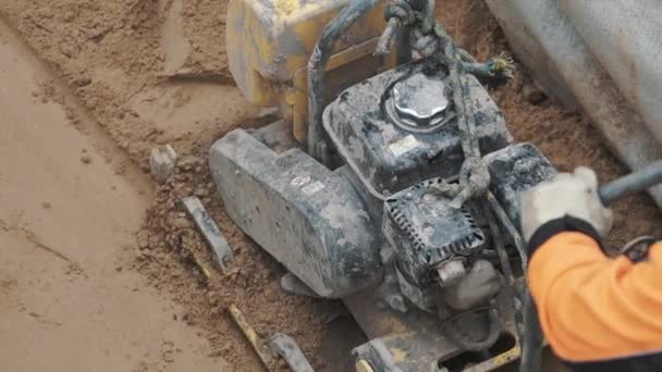 Slowmotion worker using petrol plate compactor on sand in ditch at building site — Stock Video