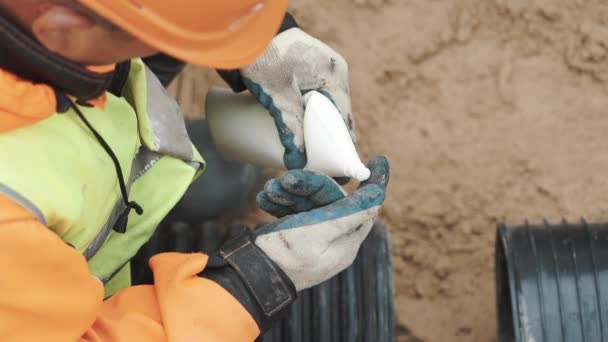 Робітник розміщує білий клей на пальці в рукавичці і наносить його на край пластикової труби — стокове відео