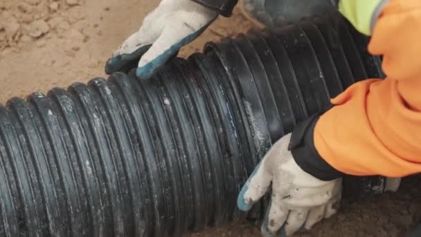 Werknemer in oranje hard muts en handschoenen zetten zwart kunststofbuizen in zand oppervlak — Stockvideo