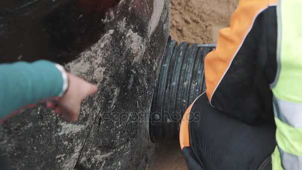 Працівник готується наносити герметик на шви чорної пластикової труби і бетонний отвір — стокове відео