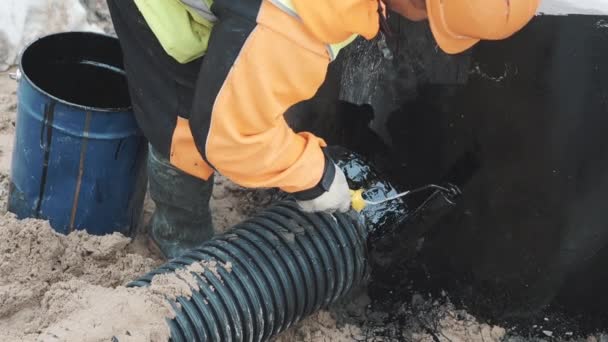 Builder sätta pitch på cement söm mellan svart plaströr och betong — Stockvideo