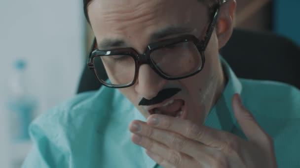Jonge mannelijke kantoorbediende in enorme glazen en grappige snorren geeuwen — Stockvideo