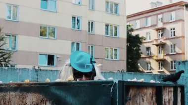 Kadın peruk içinde güneş gözlüğü, Mavi şapkalı adam çöp. Parodi. Birisi izlerken