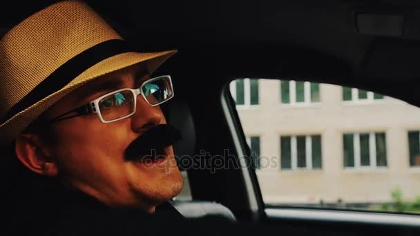Чоловік з вусами в капелюсі, окуляри сидять в машині і співають. Літній день. Веселощі — стокове відео
