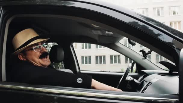 Mann mit Schnurrbart und gelbem Hut, Brille im Auto sitzend und singend. Sommer. Parodie — Stockvideo