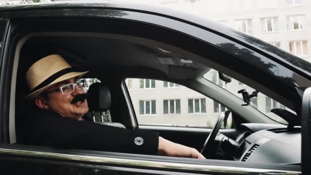 Homem com bigode em óculos sentado no carro à janela e cantar. Paródia. Diversão — Vídeo de Stock