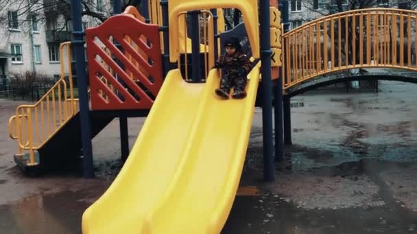 Little boy slide from hill on children playground, fall in dirty puddle. Father — Stock Video