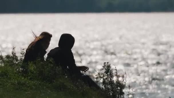Ζευγάρι κάθεται σιωπηλά στο γρασίδι μπροστά από το νερό μιας λίμνης σε μια θυελλώδη ημέρα του καλοκαιριού — Αρχείο Βίντεο