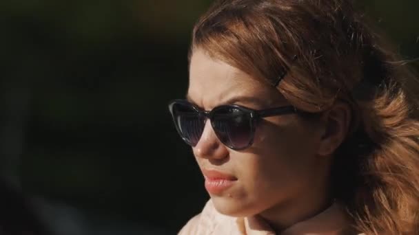 Закрыть портрет девушки в солнцезащитных очках, прищуривать глаза в летний ветреный день — стоковое видео