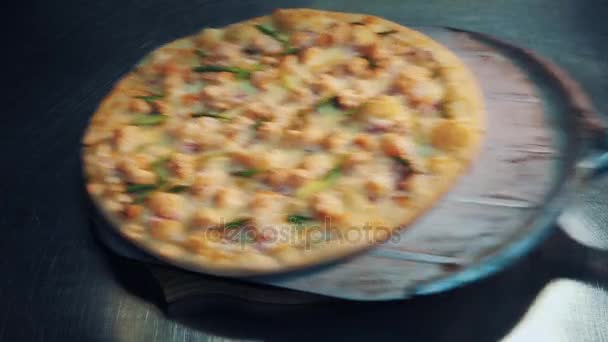 Peel tool roughly put pizza on wooden plate upon metal desk in kitchen — Stock Video