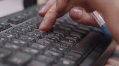 Parmakları klavyede yazarak ve kalem tutan ofis çalışanı