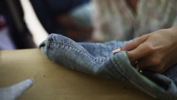 Mãos de alfaiate fêmea observa jaqueta de ganga sobre mesa de madeira oficina — Vídeo de Stock