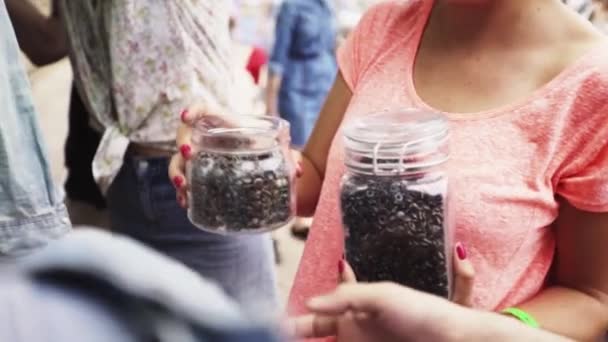 Woman gives glass jar full of metal rivets to another person at tailoring event — Stock Video