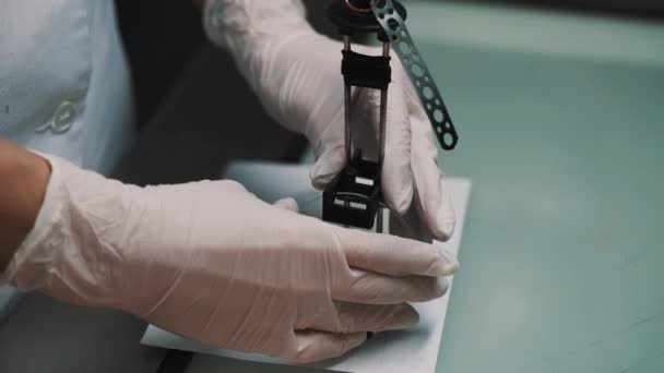 Працівник лабораторії ставить лінзи на спеціальний тримач на паперовому аркуші на столі — стокове відео