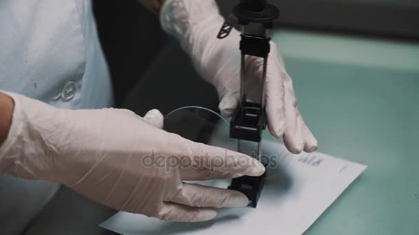Pracownik laboratorium stawia soczewki na specjalny bagażnik na arkuszu papieru na biurku tabeli — Wideo stockowe