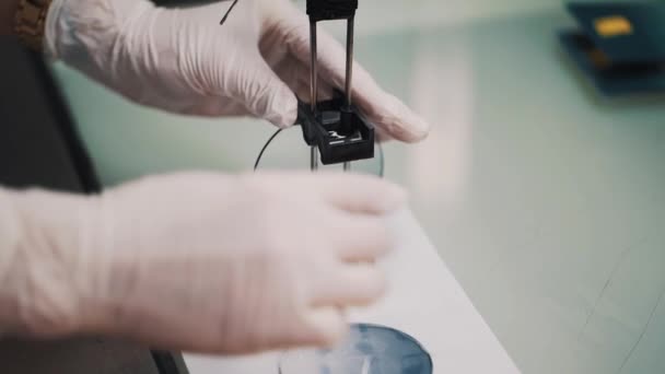 Para ilmuwan dalam sarung tangan karet menempatkan lensa kaca basah pada lembar kertas di laboratorium — Stok Video