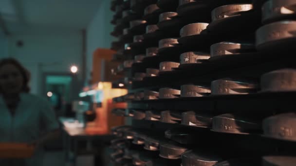 Woman with orange tray walks to shelves with stacks of metal discs — Stock Video