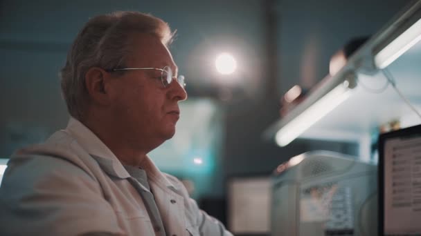 Tudós szürke hajú férfi kerek szemüveg és fehér köntöst ül a laboratóriumi — Stock videók