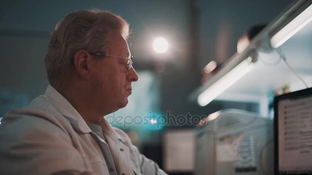 Orvosi szürke hajú férfi kerek szemüveg és fehér köntöst ül a laboratóriumi — Stock videók