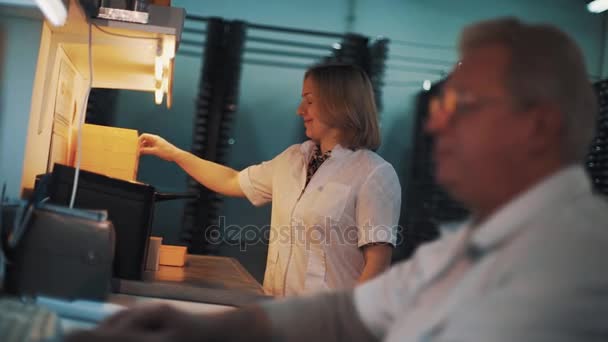 Frau in weißem Gewand verwaltet orangefarbene Plastiktabletts im Labor — Stockvideo