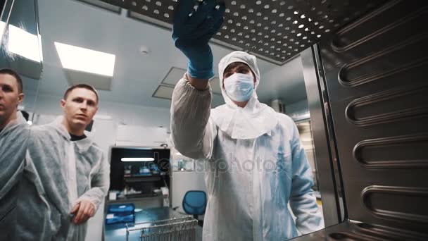 Ученый в опасном стерильном костюме вытаскивает металлический лист из печи — стоковое видео