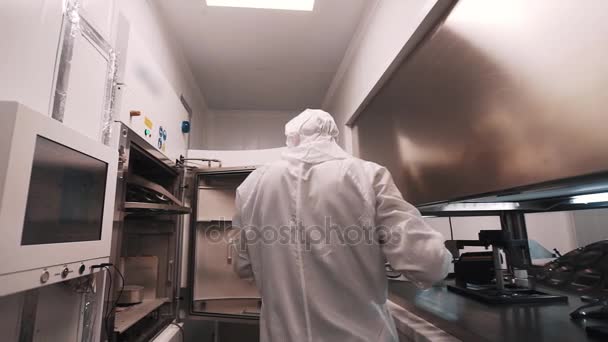 Ingeniero en bata y guantes de goma pone elemento metálico dentro del horno en laboratorio — Vídeo de stock