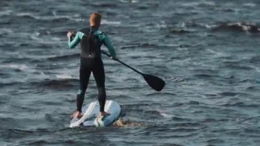 Sporcu Mavi mayo ayakta raket rüzgarlı bir günde kullanarak sörf tahtası rides