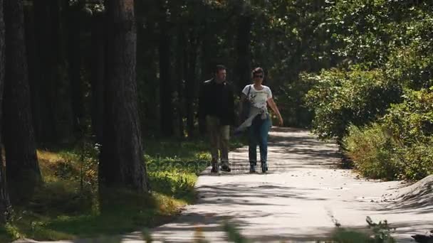 L'homme et la femme marchent vers la caméra le long d'une route asphaltée dans une forêt par une journée venteuse 