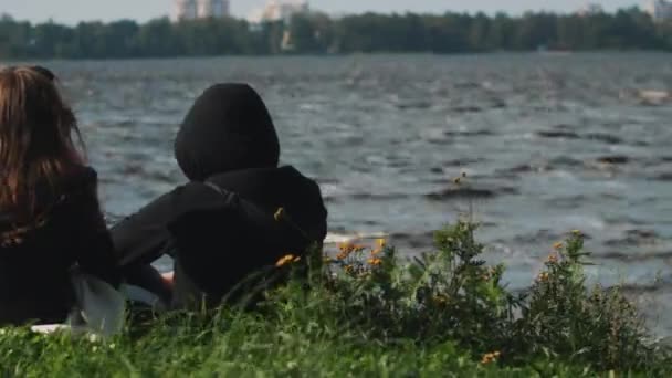 Couple assis sur l'herbe regarder comme surfeur avec pagaie promenades à travers le lac — Video