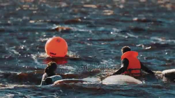 Два серфера плавают в воде рядом с досками для серфинга и оранжевым маяком. Много волн — стоковое видео