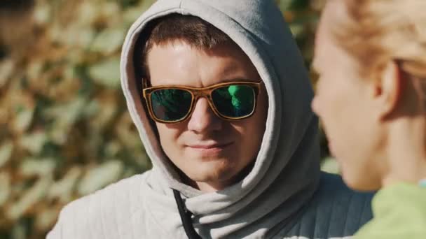 Primer plano retrato de un hombre con capucha y gafas de sol sonríe en el día ventoso de verano — Vídeo de stock