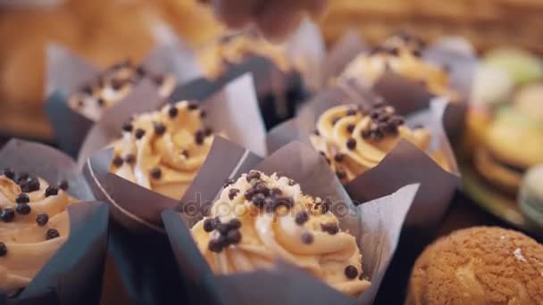 Des flocons d'amandes tombent sur la crème au beurre tourbillonnent sur des muffins dans une boulangerie — Video