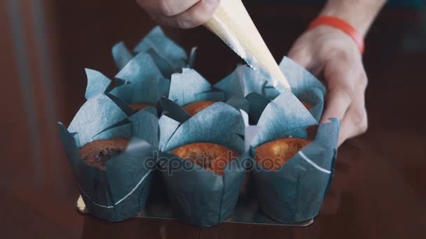 Кондитер мужские руки сжимает сладкую начинку в кексы на столе — стоковое видео