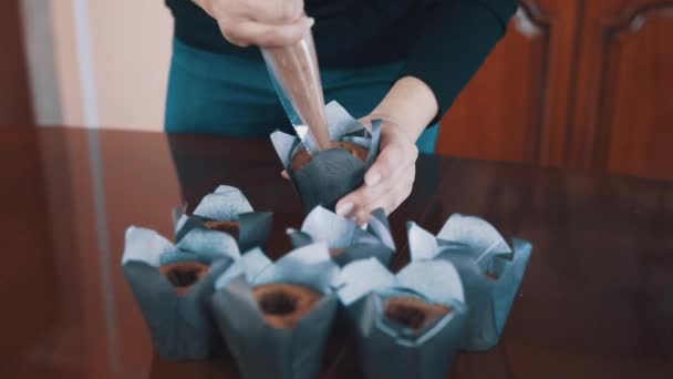 Confiseur mains féminines serre remplissage de chocolat dans des muffins sur la table — Video