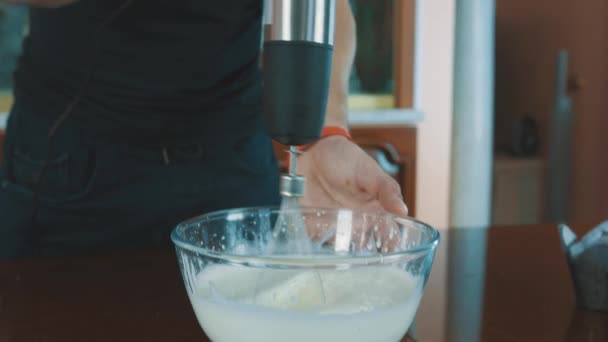 Muscular guy mixing milk in glass bowl using whisk at kitchen table — Stock Video