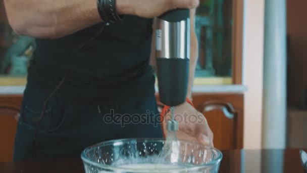 Мускулистый человек подмигивает в камеру, смешивая сливки на кухне — стоковое видео