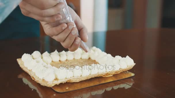 Männliche Hände des Konditors pressen Füllcreme aus Ärmel auf Kuchenschicht — Stockvideo