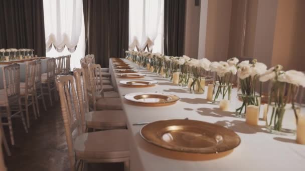 Стеклянные тарелки и вазы с розами на банкетном столе в роскошном зале — стоковое видео