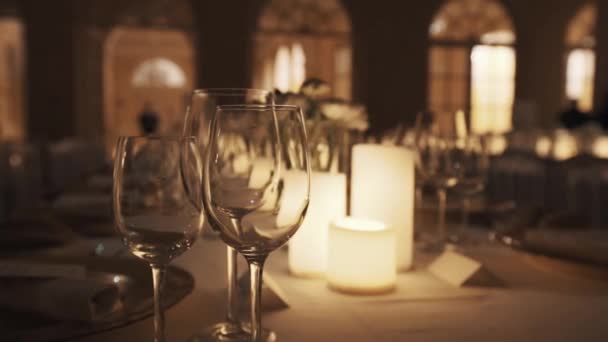 Vaciar vasos de vino en la mesa con velas encendidas y platos en la sala de banquetes — Vídeos de Stock