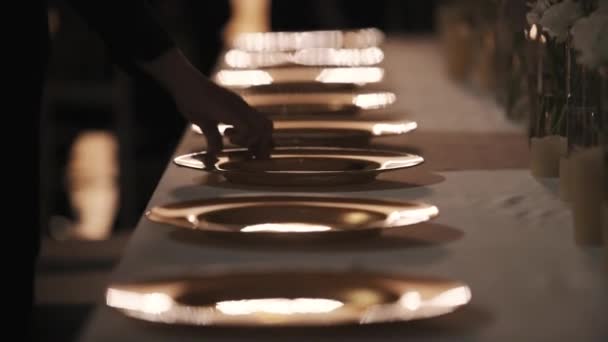 Рука официанта кладет вилки возле тарелок на банкетный стол в полутёмной комнате — стоковое видео