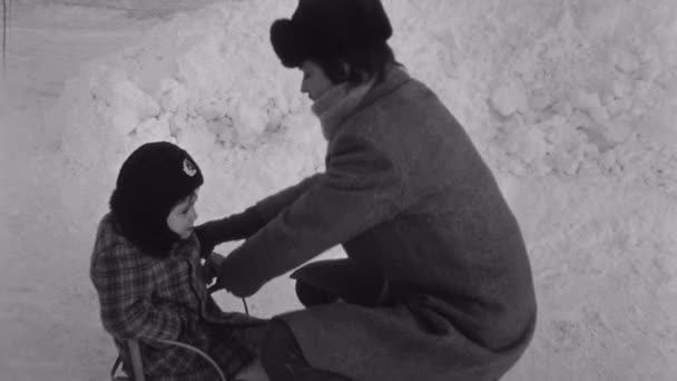 СЕНТ-ПЕТЕРБУРГ, РОССИЯ, 1981: Старая винтажная черно-белая киносемья, гуляющая по зимнему городу, ребенок на санях — стоковое видео