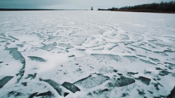 Bevroren meer verbrijzelde ijs oppervlak bedekt met sneeuw, ruïneerde Voortbouwend op oever — Stockvideo