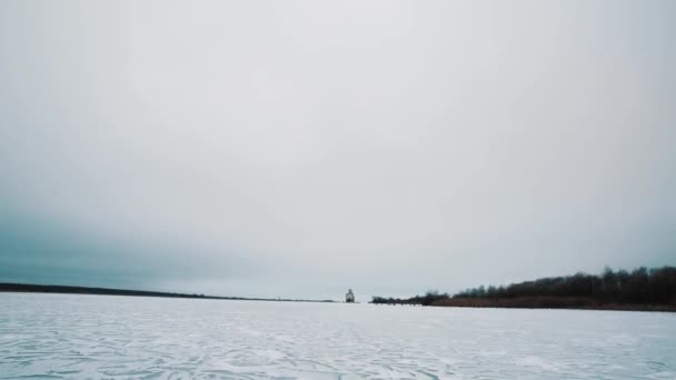 Bevroren rivier verbrijzelde ijs oppervlak bedekt met sneeuw, verlaten gebouw op oever — Stockvideo
