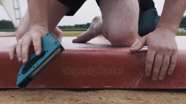 Hombre en pantalones cortos pone material rojo en la construcción del escenario utilizando grapadora — Vídeos de Stock