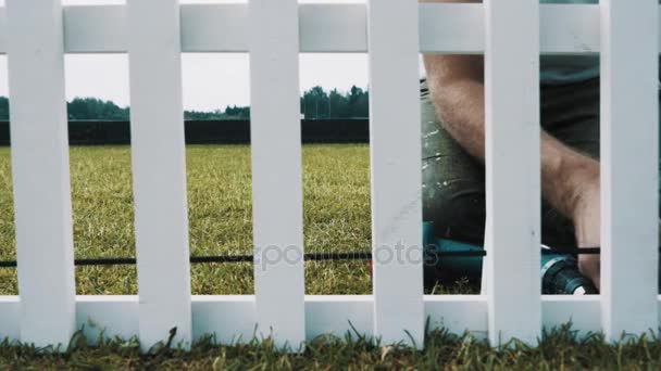 Деревообработчик строит белый деревянный английский забор на зеленой газоне травы — стоковое видео