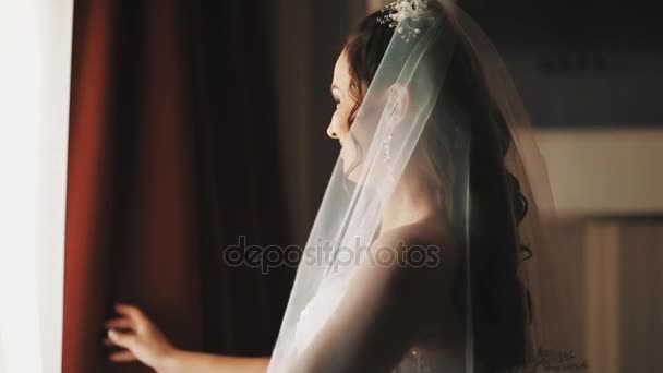 Jonge bruid vrouw in bruiloft jurk flyes open gordijnen in halve donkere kamer — Stockvideo