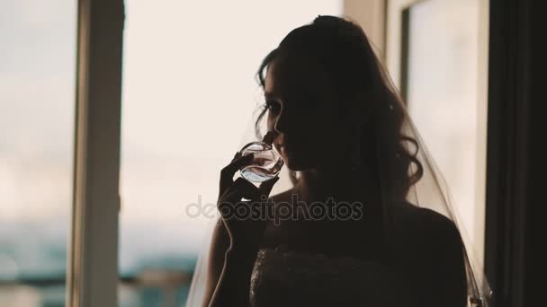 Joven novia en vestido de novia olfatear y applyes perfume en frente de la ventana — Vídeos de Stock