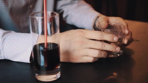 Руки человека в клетчатой рубашке, держащего стакан виски на столе в баре — стоковое видео