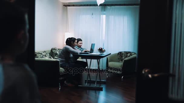 Joven niño observa como la mujer y el hombre utilizando la computadora en la sala de estar, habla con papá — Vídeos de Stock