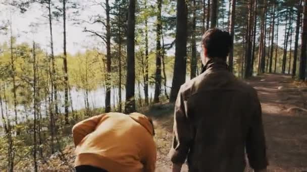 Man pikt rock en gooit het in meer tijdens het wandelen in het bos met vriend — Stockvideo